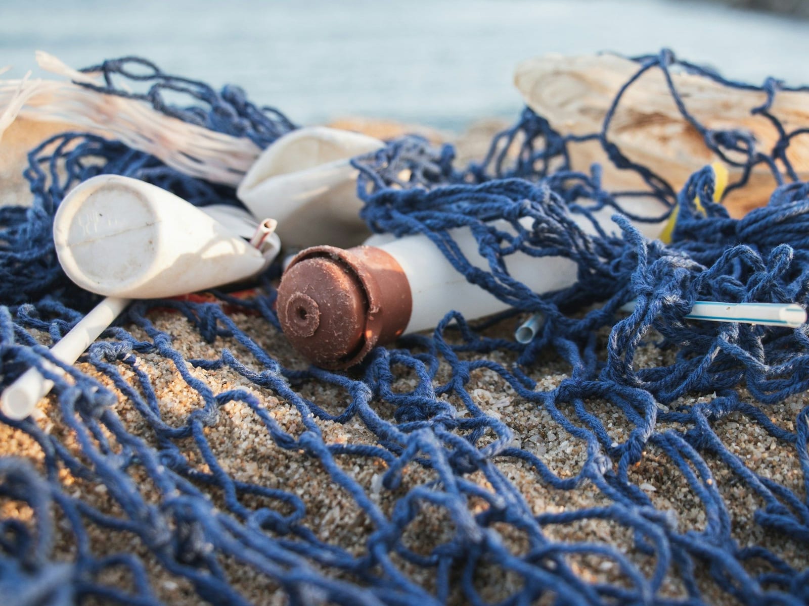 砂浜に打ち上がった青い漁網にからまったプラスチックの容器