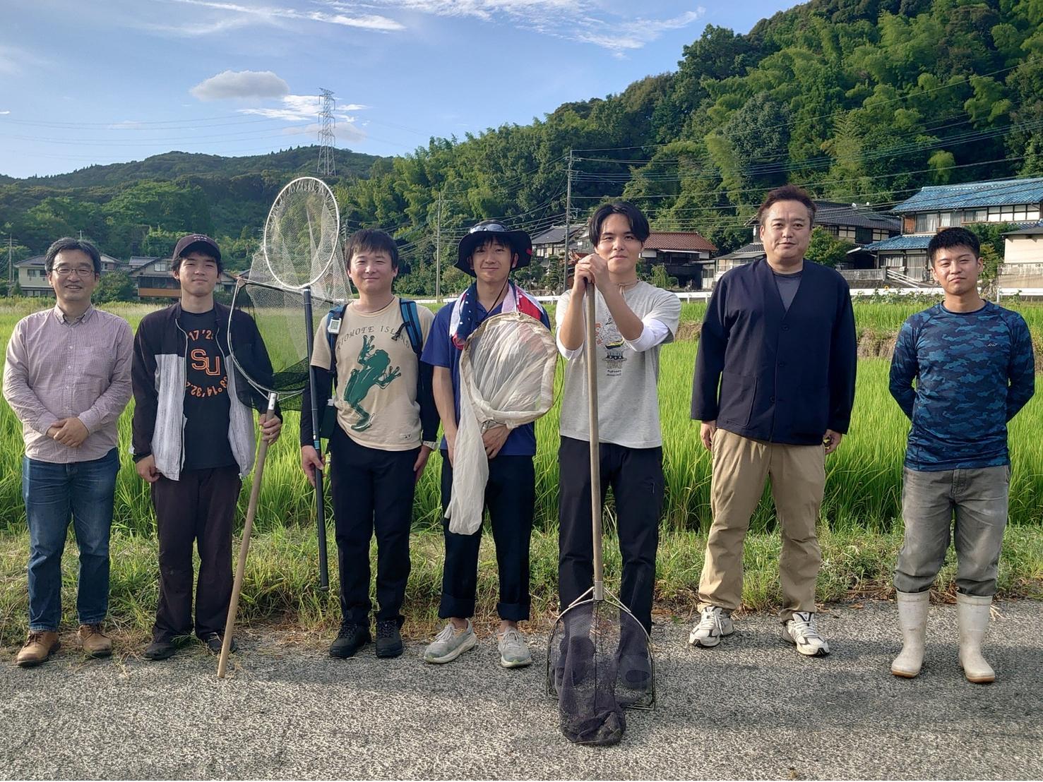青々とした横枕の田んぼの前で、タモ網や捕虫網を手に並ぶ生物調査のメンバー