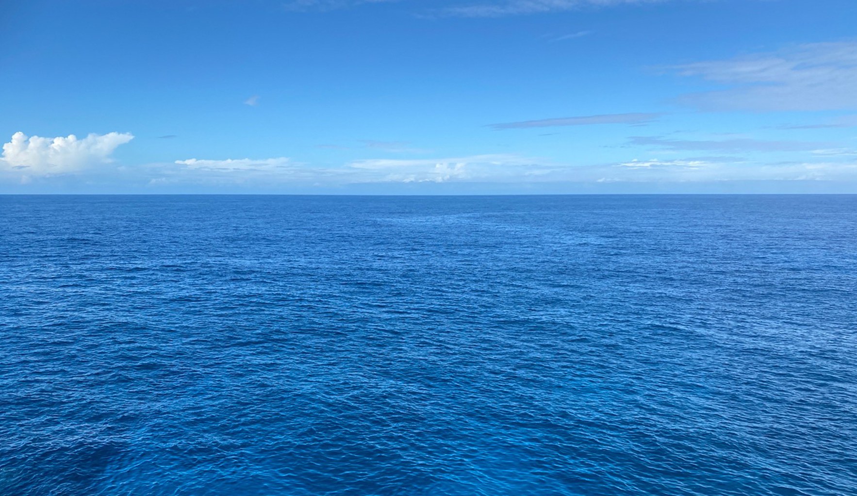 Blue sea stretching to the horizon under a sky with white clouds
