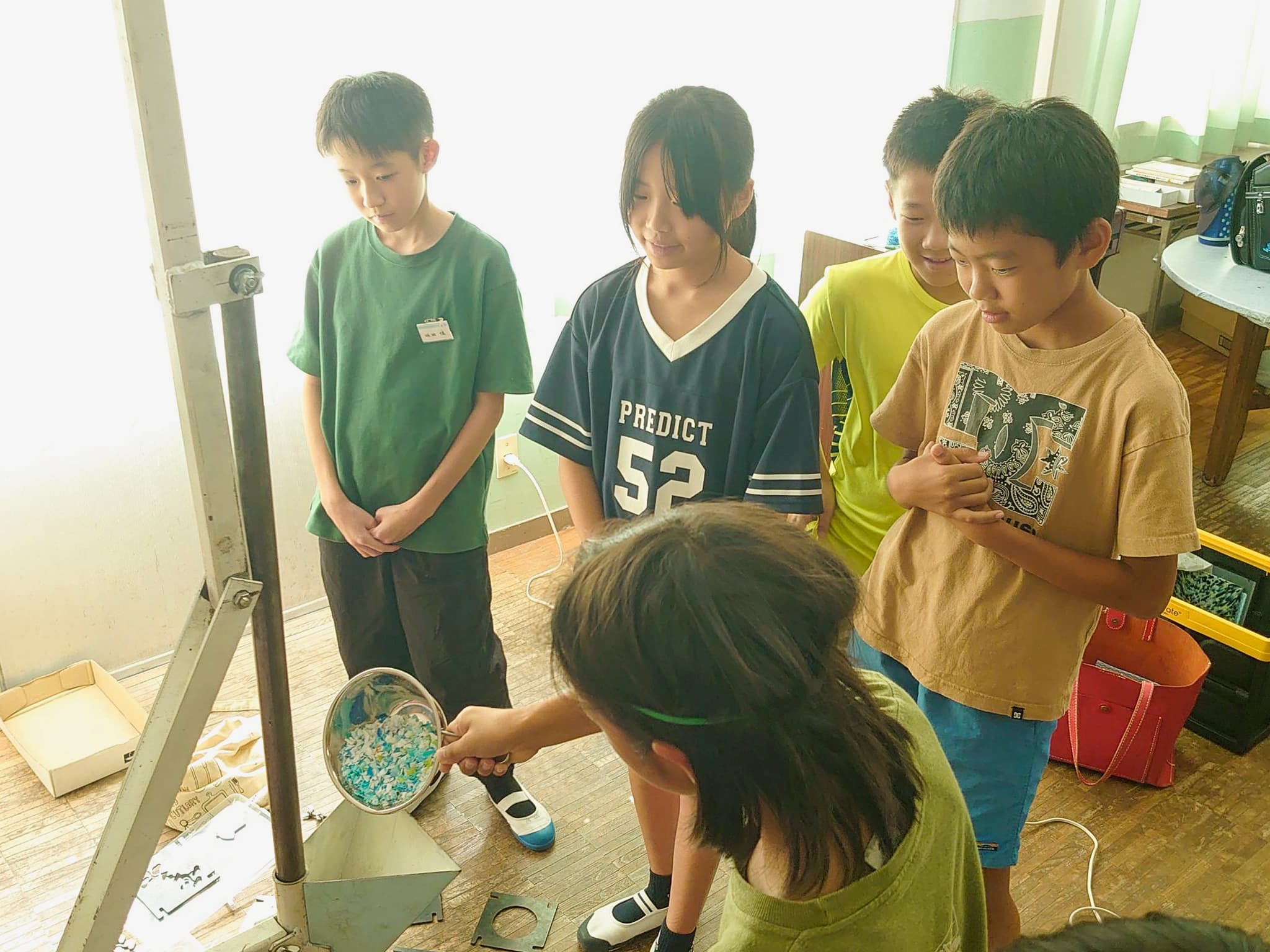 ペットボトルキャップを射出成型機に入れる児童たち