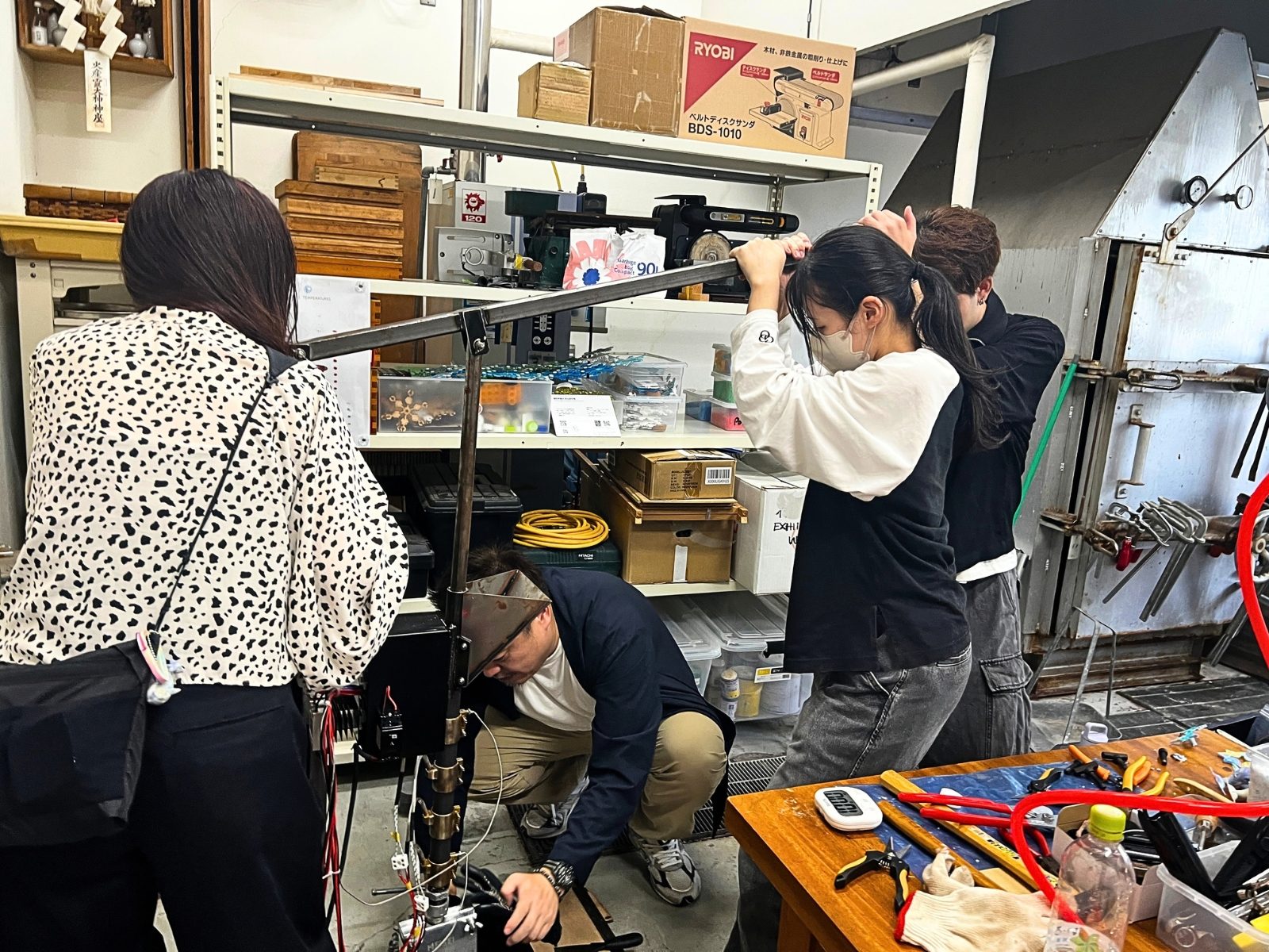 倉敷芸術科学大学の工房で、射出成形機を囲んで作業するプラ芸の学生たち