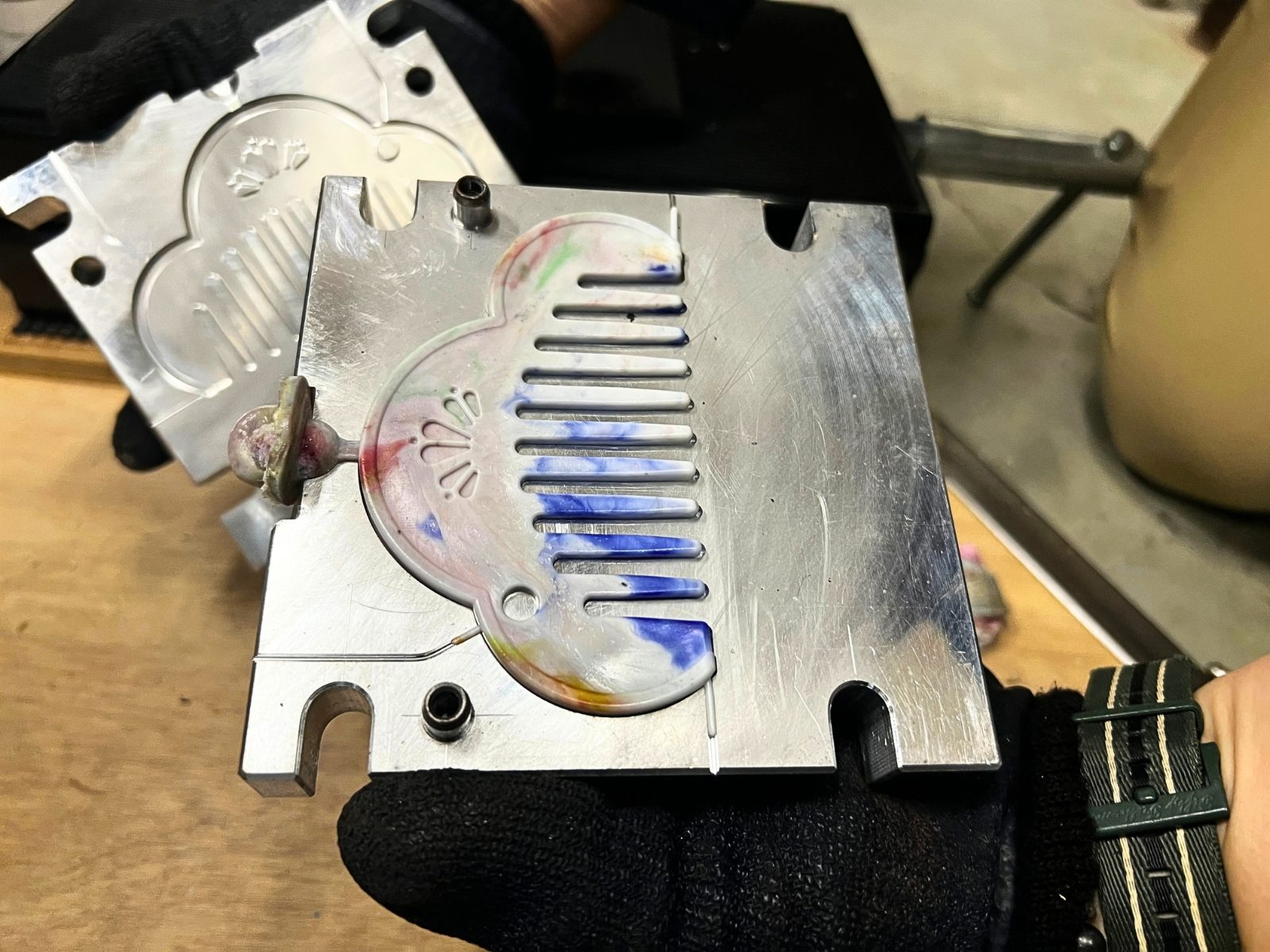 開いたアルミの金型の中に、青と白のマーブル模様で成形された松モチーフの櫛