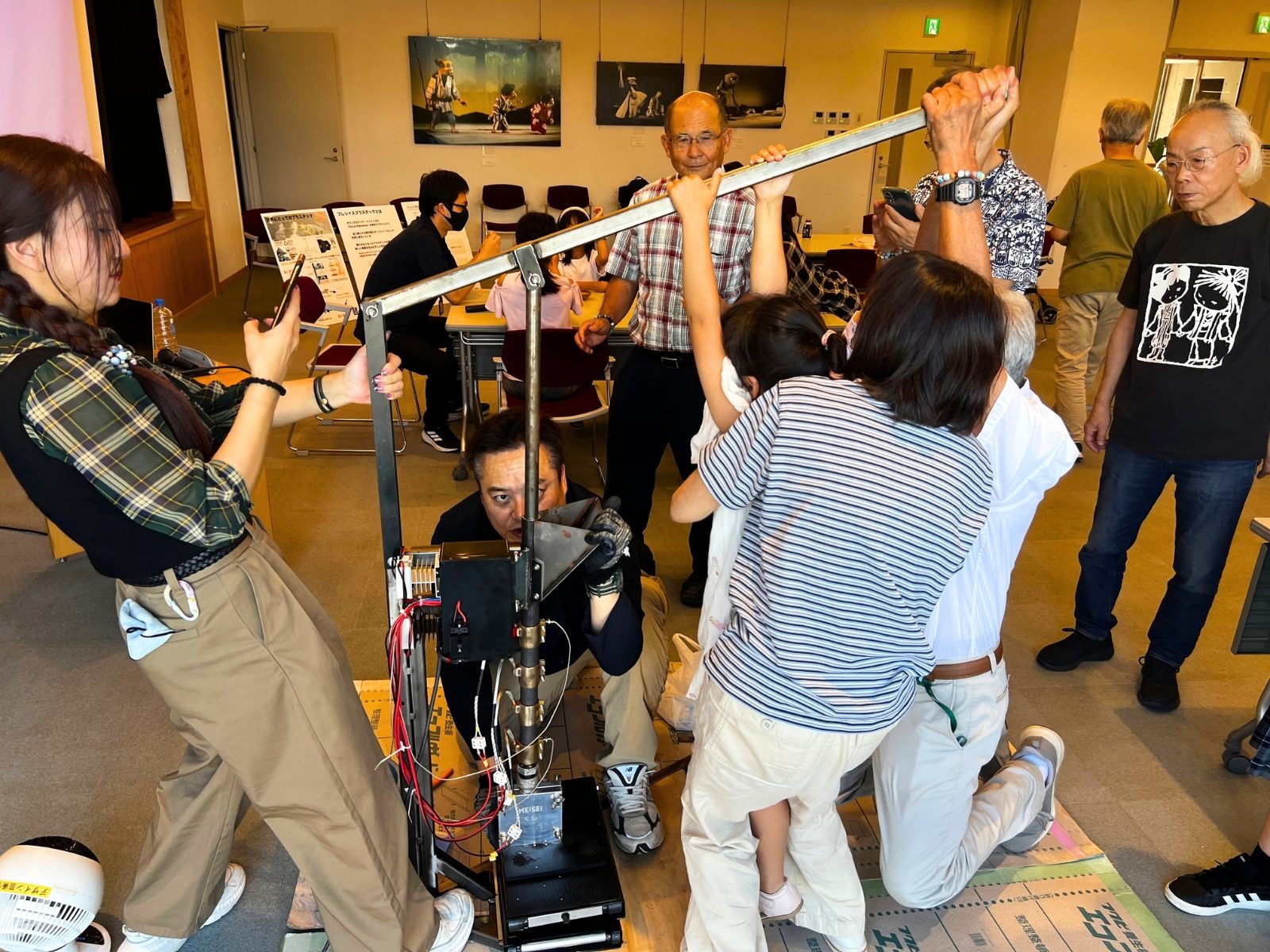 図書館の会場で、射出成形機のレバーを押し下げる参加者と、それを見守る人たち
