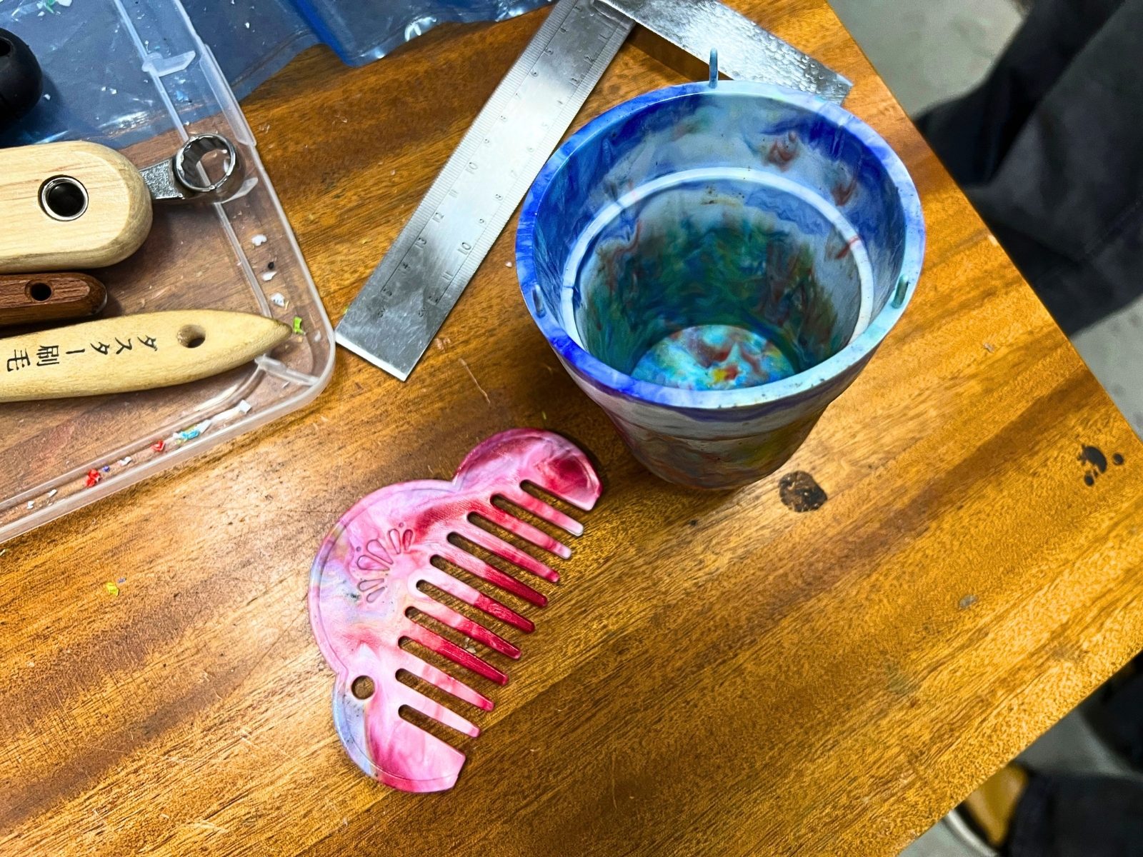 作業台の上に置かれた、ピンクのマーブル模様の櫛と、青緑のマーブル模様の小さなカップ