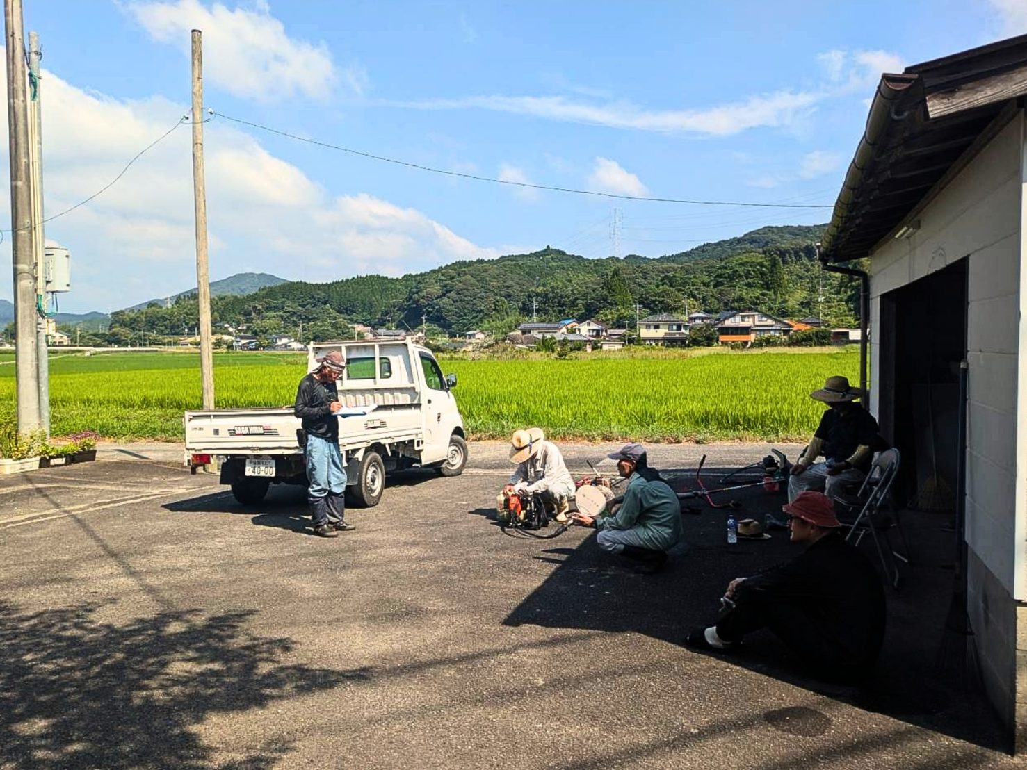 作業の合間、小屋の日陰で刈払機の手入れをしながらひと休みするみなさん