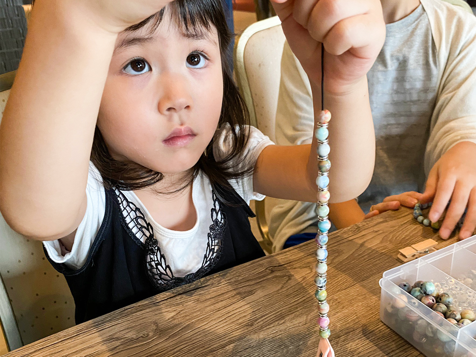 ワークショップのテーブルで、マーブル模様のビーズのブレスレット作りをする女の子