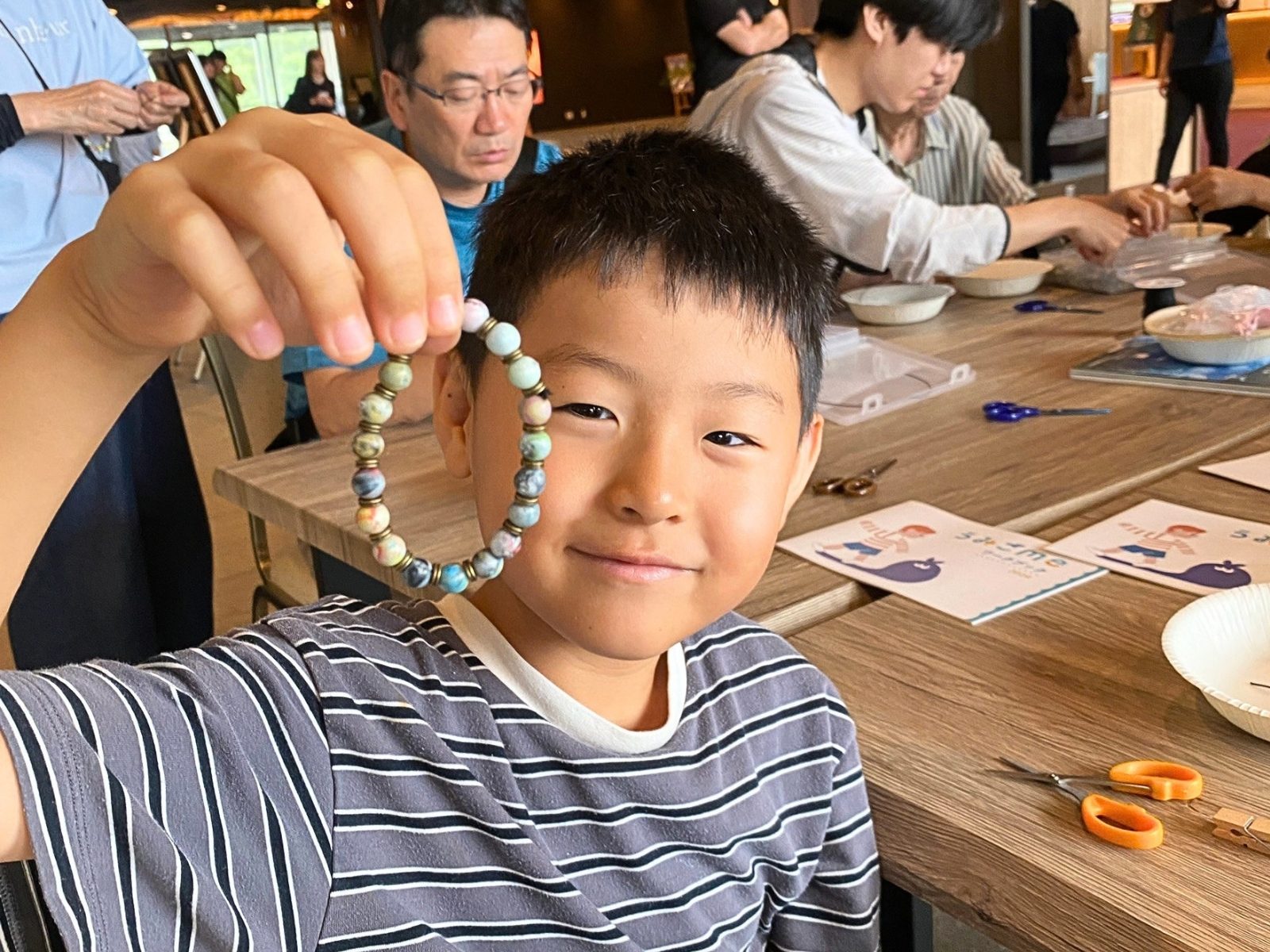 自分でつくったリサイクルプラスチックビーズのブレスレットを掲げて見せる男の子