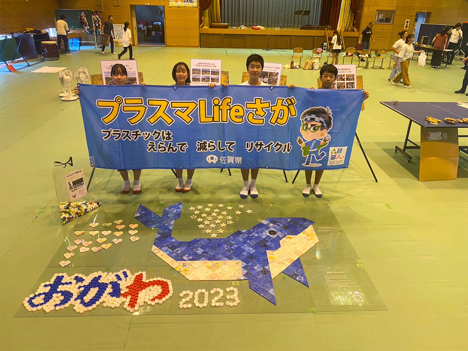 2023年 完成したクジラの海ごみアートとプラスマLIFEさがの横断幕を持つ生徒たち