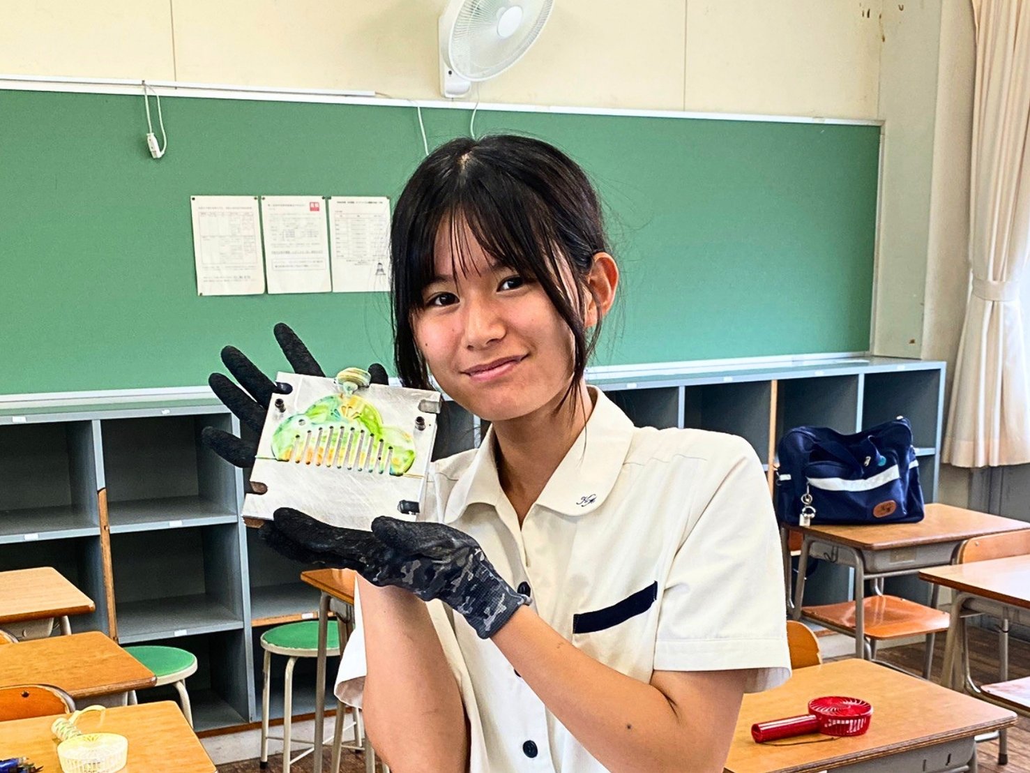 成形したばかりの緑のマーブル模様の櫛を手に微笑む生徒