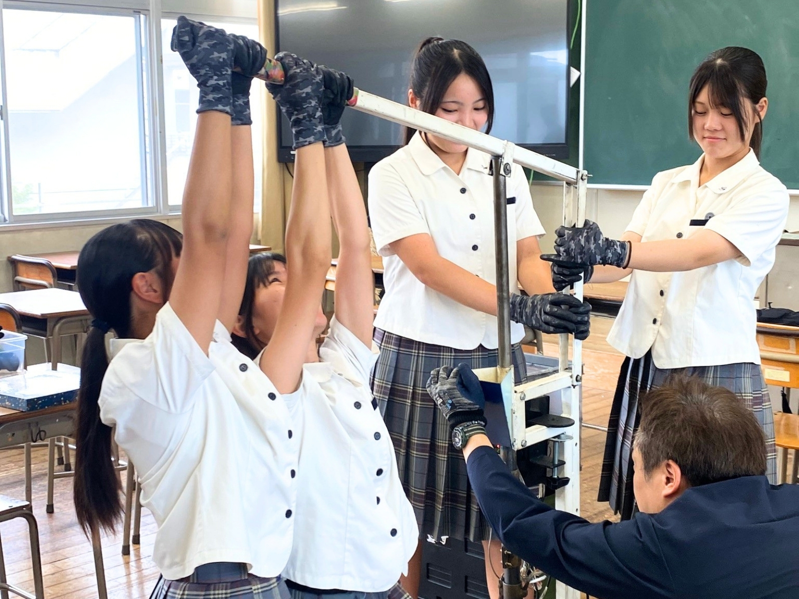射出成形機のレバーを、生徒たちがみんなで力を合わせて引き下ろす様子