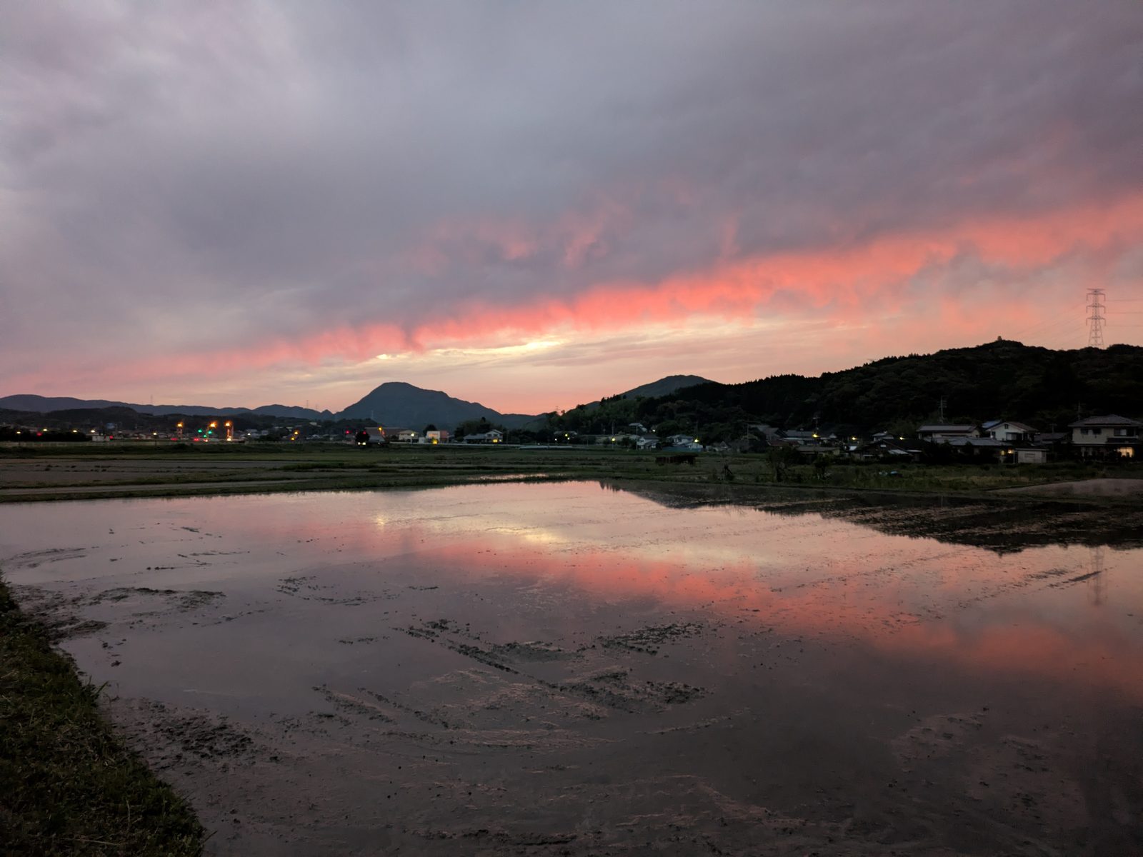 夕焼け空と山並みを映す、水を張った田んぼ