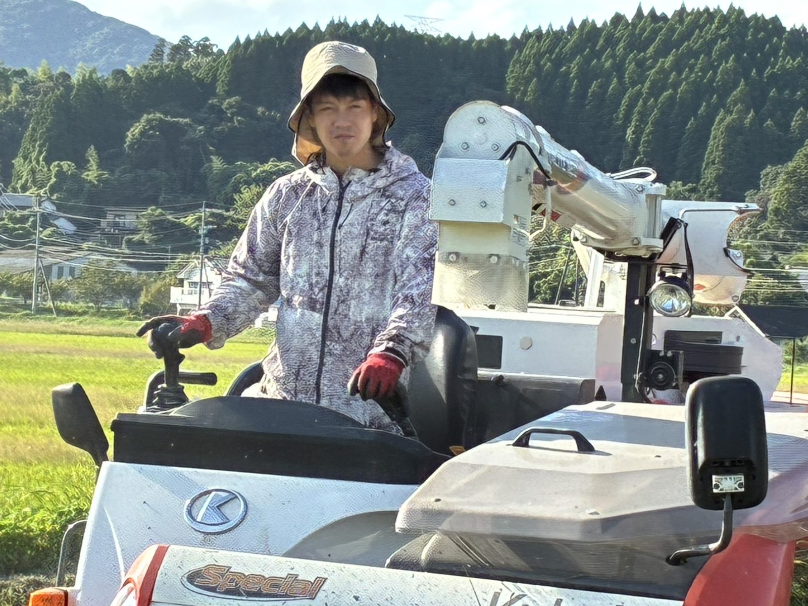山を背に、コンバインに乗って稲刈りをする様子