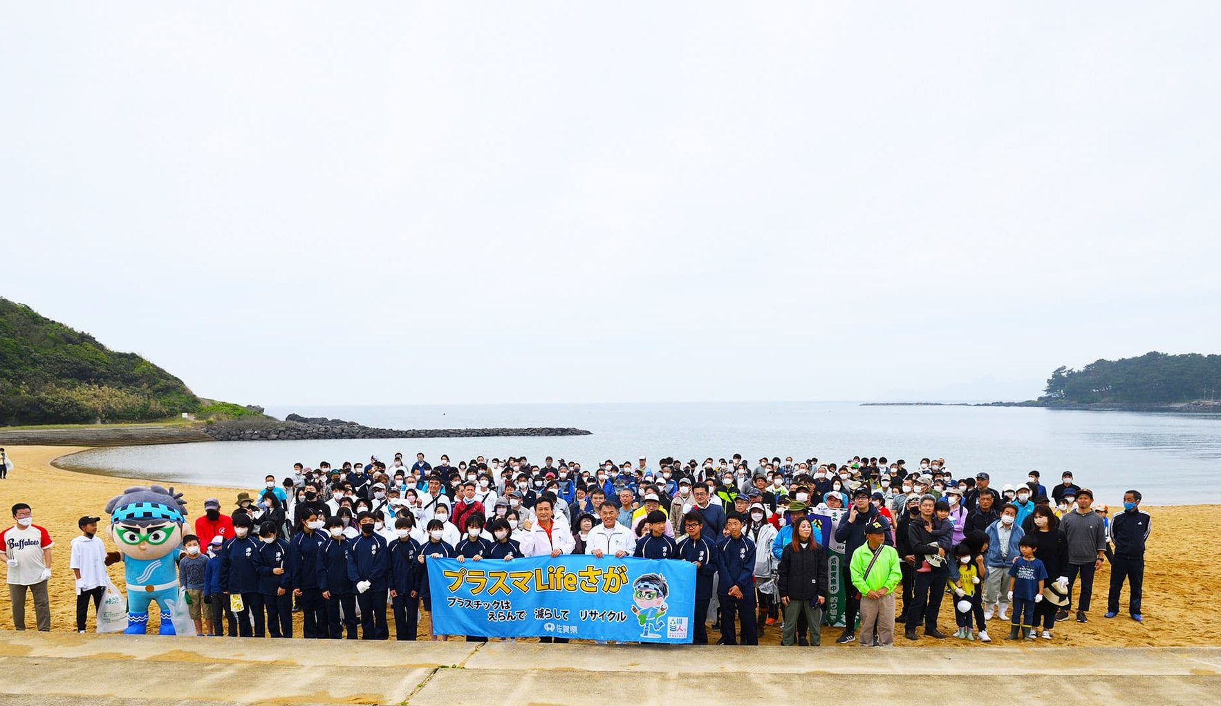 Beach cleanup participants holding a banner on the sand at Hado Misaki, Karatsu, Saga, with the sea behind them