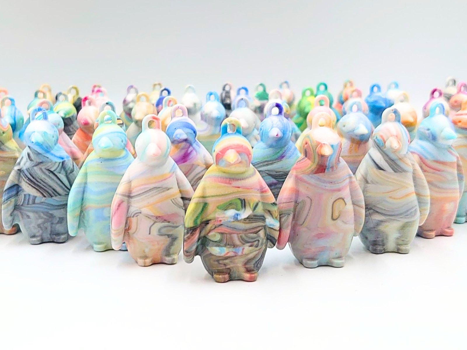 Many marbled penguin keychains made from collected plastic bottle caps, laid out side by side