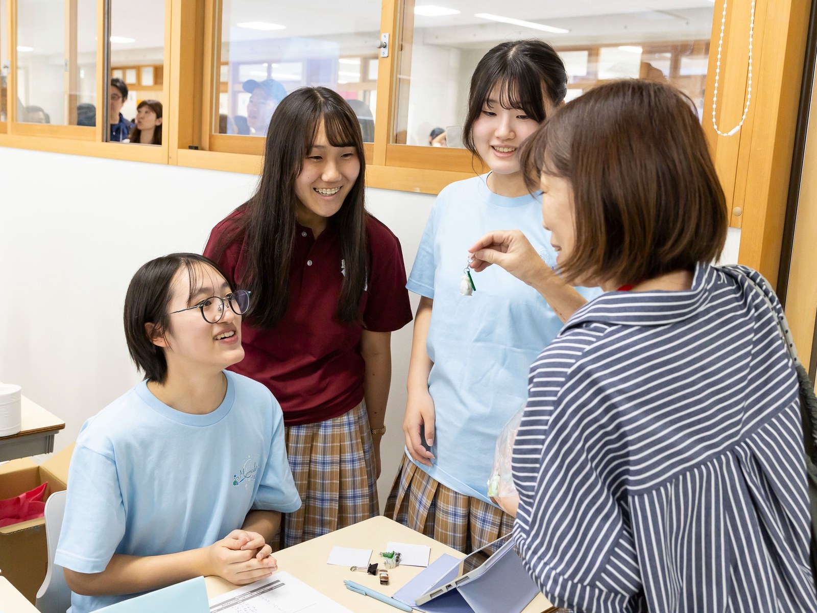 販売ブースで、来場者がキーホルダーを手に取り、生徒3名が笑顔で話しかけている