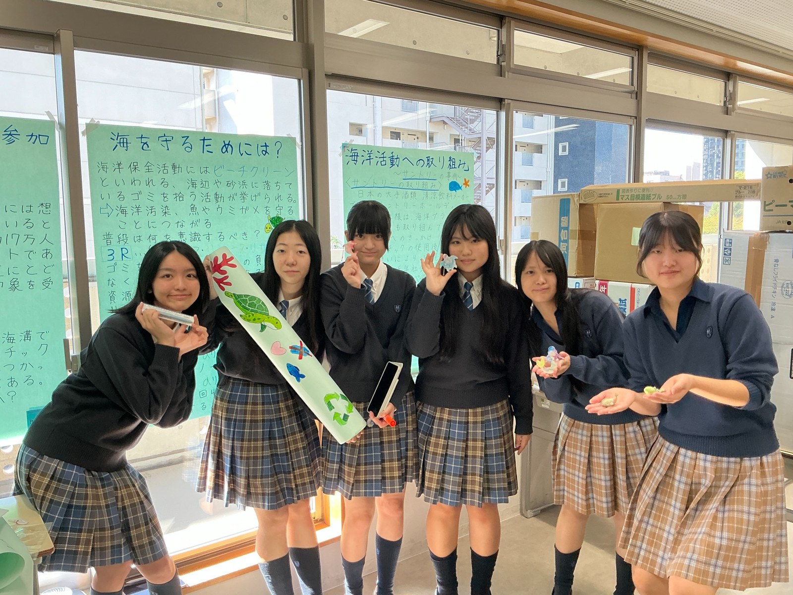 海の展示の模造紙の前で、キーホルダーを手のひらにのせて見せる制服姿の生徒6名