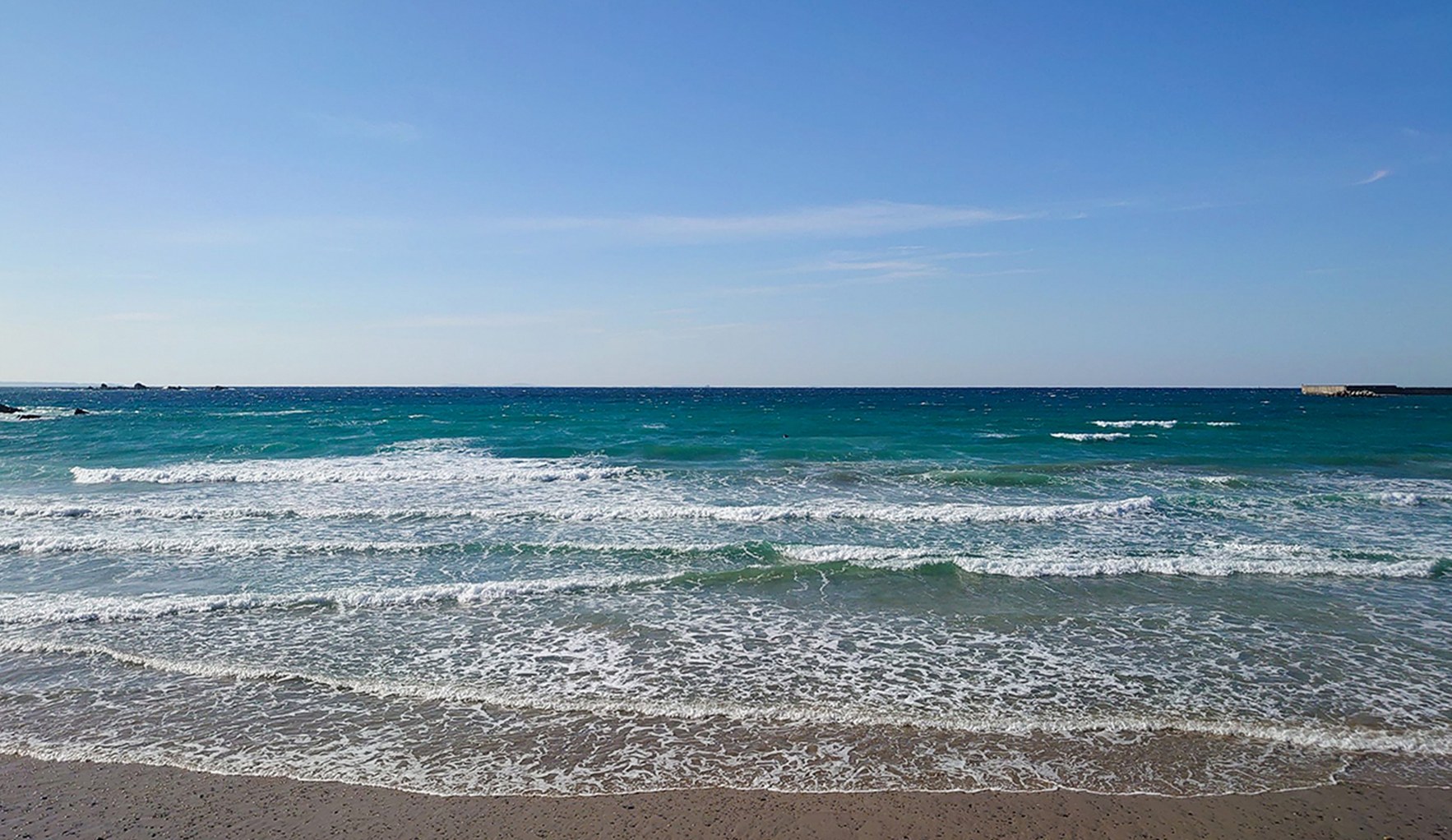 砂浜に白い波が打ち寄せる晴れた日の海