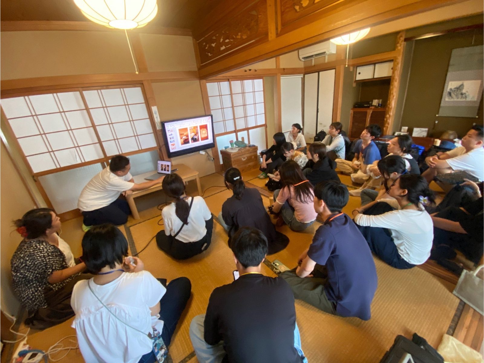 和室いっぱいに座って、モニターのスライドを見ながら講義を聞く参加者たち