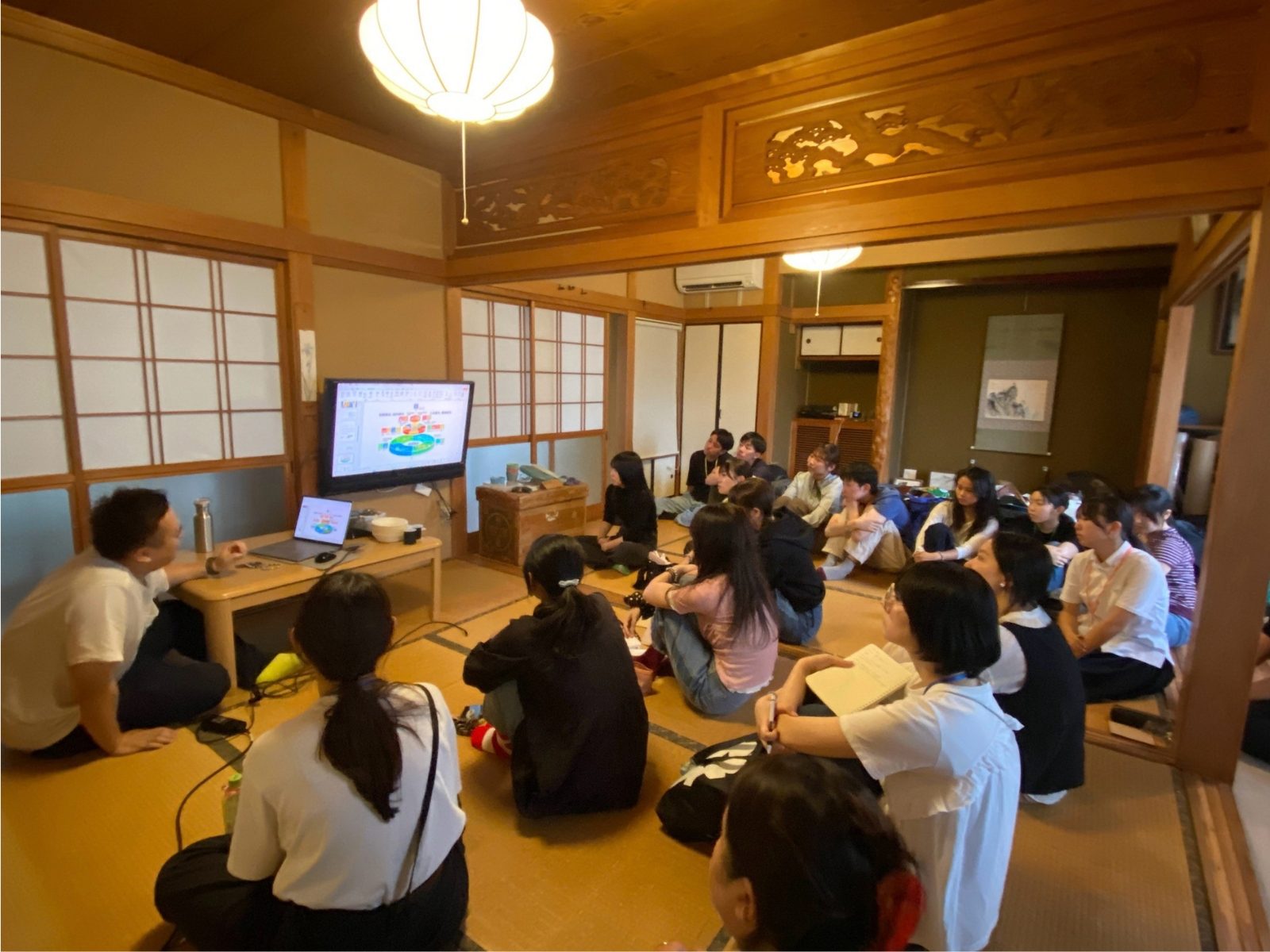 和室の会場で、モニターに映したスライドを前に座って講義を聞く参加者たち