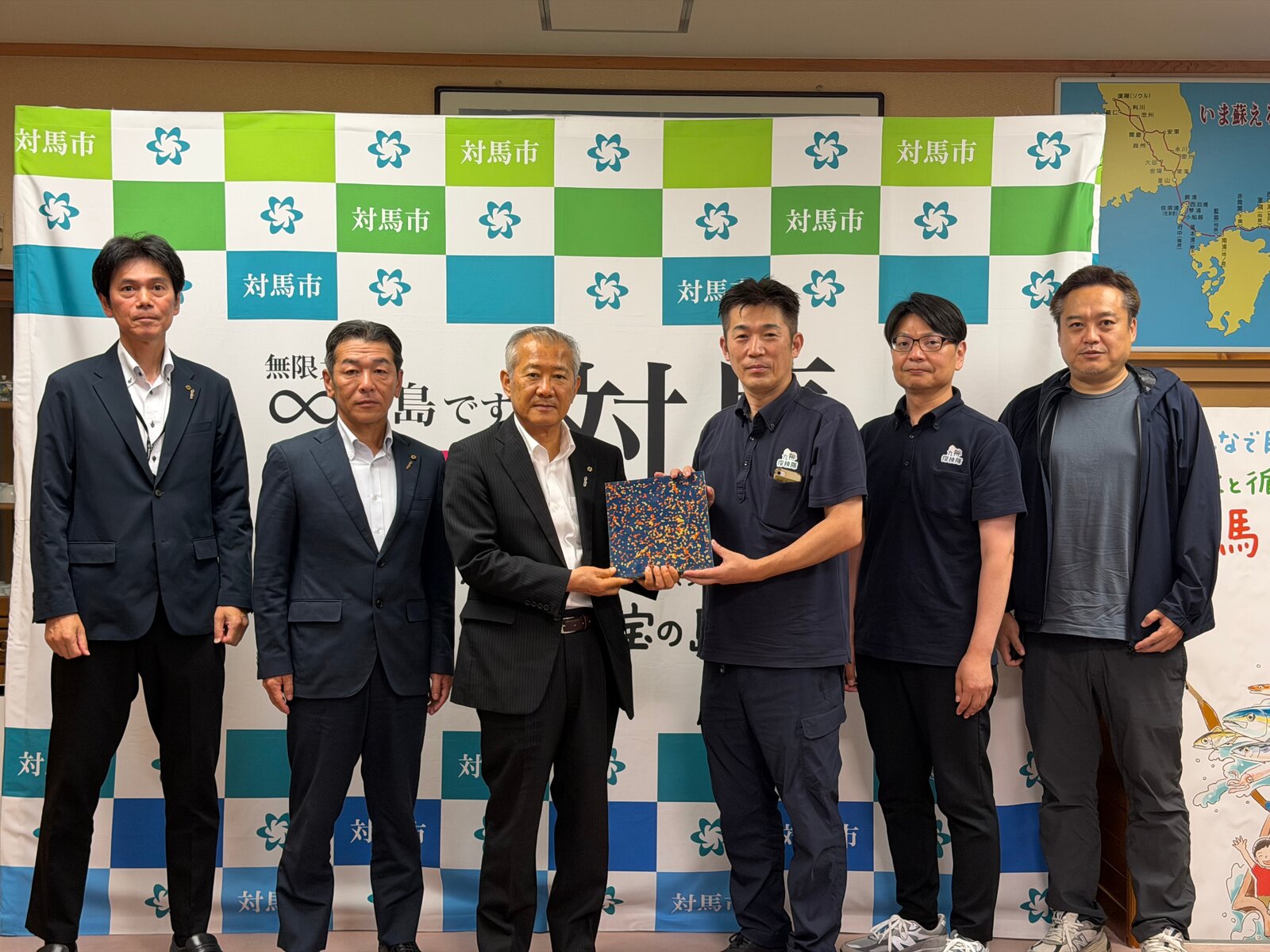 対馬市庁舎で、対馬の海洋プラスチックから生まれたシート建材を手にするプロジェクトの仲間たち